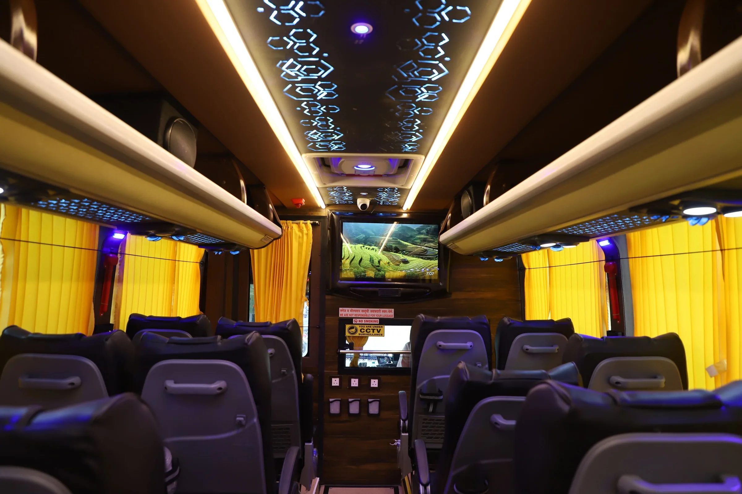 Bus interior with passenger seats, aisle, ceiling lights, TV, CCTV and curtains